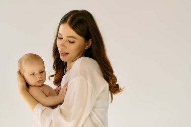 Genç bir anne bebeğini nazikçe kucaklar, ikisi de neşeli ve samimi bir bağ paylaşır..