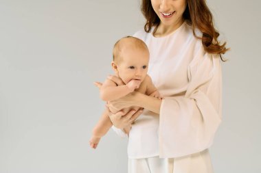 Güzel, genç bir anne bebeğiyle birlikte neşeyi kutlarken sakin, yumuşak bir atmosferde güler..