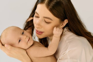 Genç bir anne gülümseyen bebeğini kucağında tutar, aile mutluluğunu yansıtan sevgi dolu bir anı paylaşır..