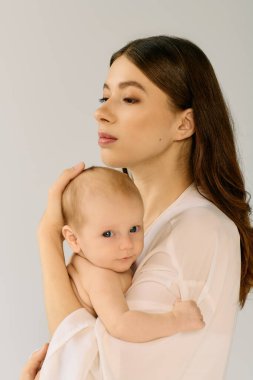 Güzel, genç bir anne bebeğini kucağında tutuyor. Sakin bir atmosferde sevgi ve sıcaklık yayıyor..