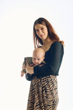 Neşeli genç bir anne, tatlı bebeğini yanında tutar. Huzurlu bir ortamda sıcaklığını ve sevgisini yayar..