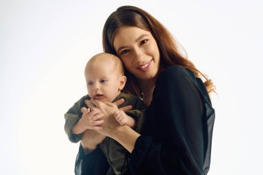 Genç bir anne, neşeli çocuğunu kucaklar. Evdeki bağlarını ve mutluluklarını gözler önüne serer..