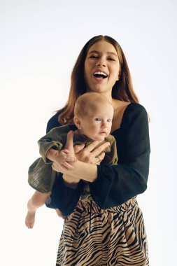 Neşeli genç bir anne çocuğunu kucağına alır, parlak bir boşlukta sevgi saçar..