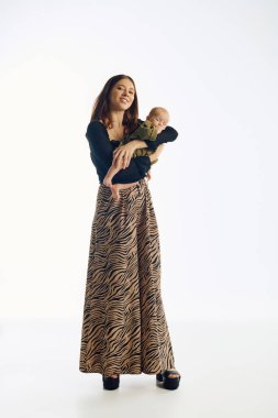 Genç bir anne, bebeğini neşeli bir ortamda nazikçe tutarken sevgiyle gülümser..