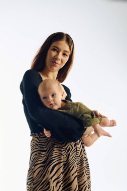 Genç anne sevgiyle bebeğini kucağında tutuyor ve çağdaş bir ortamda sıcak bir bağ kuruyor..