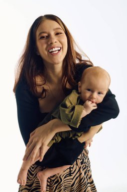 Neşeli genç bir anne çocuğunu kucağında tutuyor, sevgi ve bağ yayıyor..