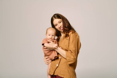 Güzel, genç bir anne, bebeğini sıcacık ve huzurlu bir ortamda sevgiyle tutarken gülümser..