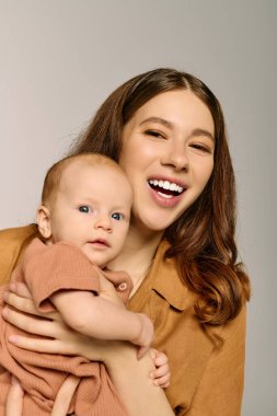 Gülümseyen genç bir anne çocuğunu kucaklar, saf bir sevinç anı yakalar..