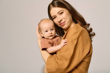 Genç bir anne, bebeğini sıcacık ve samimi bir ortamda tutarken sıcak bir şekilde gülümser..