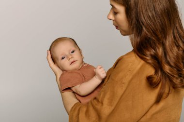 Güzel, genç bir anne, küçük çocuğunu kollarına alır, sıcaklık ve neşe saçar..