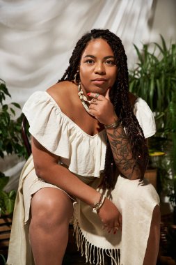 Saçları örgülü kendine güvenen bir kadın yemyeşil bir elbiseyle düşünceli bir şekilde oturur.