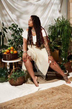 Saçları örgülü güzel bir kadın, bereketli bitkilerle çevrili bir yaz elbisesi içinde zarif bir poz verir..