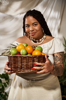 Güzel bir kadın canlı bir stüdyoda taze meyvelerle dolu bir sepet sergiliyor..
