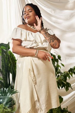 Saçlı güzel bir kadın canlı yeşil bitkilerin arasında yaz elbisesi içinde poz veriyor, neşe saçıyor..