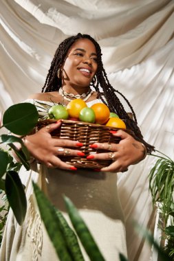 Neşe saçı örgülü Afrikalı Amerikalı bir kadın elinde yeşil meyvelerle dolu bir sepet tutuyor..