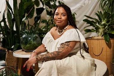 Örgü ören afro-amerikalı kadın canlı iç mekan bitkileri arasında zarifçe poz veriyor..