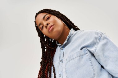 Saçları örgülü güzel bir Afro-Amerikalı kadın şık bir kot giysisiyle rahatça poz veriyor..