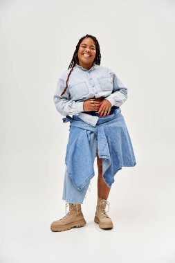 Saçları örgülü neşeli bir Afrikalı Amerikalı kadın, kotlarını bir stüdyo ortamında sergiliyor..