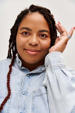 Kendine güvenen bir kadın şık bir kot elbiseyle neşeli bir poz verir, güzel örgüleri vardır..