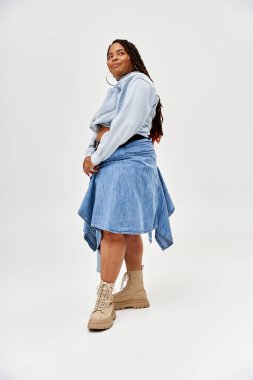 Göz kamaştırıcı bir Afrikalı Amerikalı kadın, gri bir arkaplana karşı kot elbiseyle zarifçe poz veriyor..