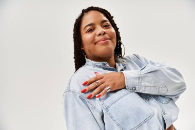 Saçları örgülü canlı bir Afrikalı Amerikalı kadın gri bir arka plana karşı duruyor..