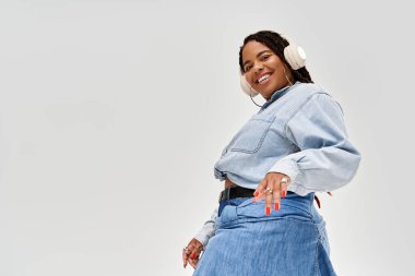 Saçı örgülü, kendine güvenen bir kadın stüdyo ortamında şık bir kot elbise giyiyor, neşe saçıyor..