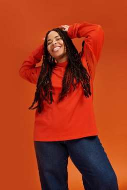 Saçları örgülü şık bir Afro-Amerikalı kadın canlı kıyafetiyle poz vermekten zevk alıyor. Mutluluk saçıyor..