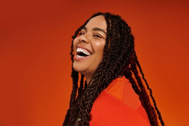 Saçları örgülü neşeli bir genç kadın neşeli bir şekilde poz veriyor, neşeli ruhunu sergiliyor..