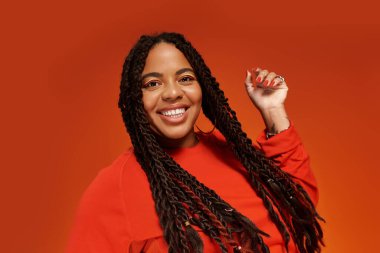 Güzel bir Afrikalı Amerikalı kadın parlak turuncu bir ortamda mutlu bir şekilde gülümsüyor..