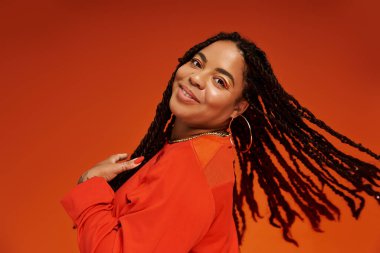 Saçları örgülü şık bir kadın parlak turuncu bir elbise içinde mutluluk saçıyor..