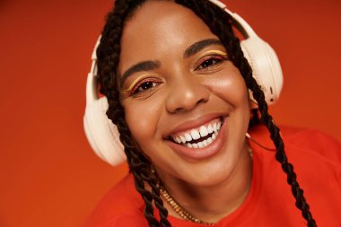 Parlak kulaklıklı neşeli bir Afrikalı Amerikalı kadın canlı turuncu bir arka plana karşı poz veriyor..