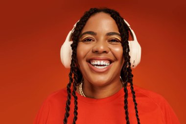 Saçları örgülü, şık bir kıyafet giyerken ışıl ışıl gülümseyen Afro-Amerikalı bir kadın..