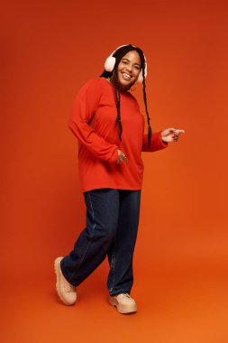 Afro-Amerikalı şık bir kadın parlak turuncu bir arkaplanda neşe içinde poz veriyor..