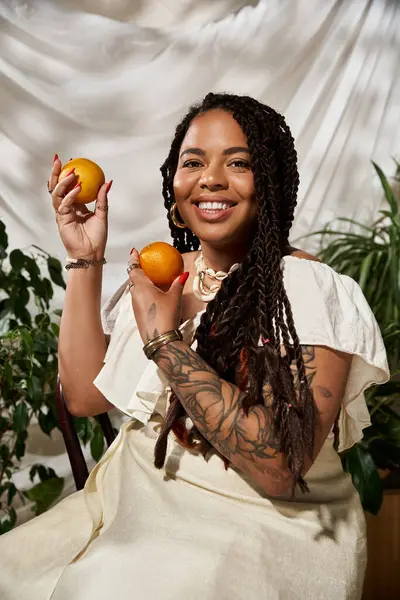 Örgülü neşeli bir Afrikalı Amerikalı kadın canlı bitkiler arasında portakallarla poz veriyor..