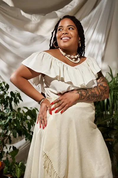 Güzel bir Afrikalı Amerikalı kadın şık bir yaz elbisesi içinde poz veriyor. Etrafında canlı bitkiler var..