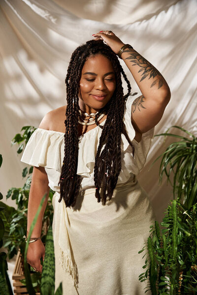 A pretty African American woman in a summer dress poses amidst green plants, exuding bliss.