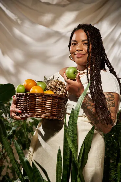 Örgülü Afrikalı bir Amerikalı kadın neşe içinde bir sepet taze meyve ile poz veriyor..