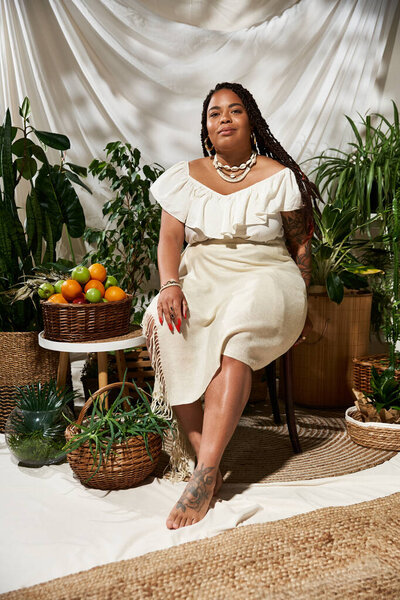 A confident African American woman with braids enjoys a sunny moment surrounded by green plants.