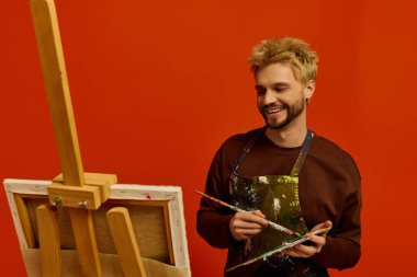 Yakışıklı genç adam yaratıcılıkla dolu canlı bir stüdyoda resim yaparken gülümsüyor..