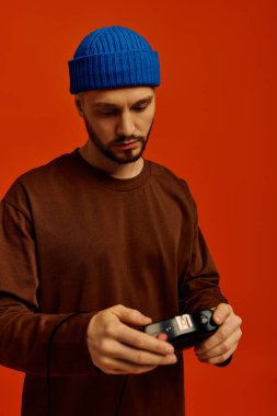 Kahverengi kazaklı ve mavi bereli genç bir adam, derin düşüncelere dalmış, klasik bir cihazla nişanlanmış..