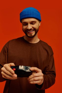 Parlak renkli arka plan, kamerasını tutarken gülümseyen yakışıklı bir genci ön plana çıkarıyor..