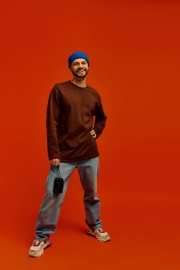 Yakışıklı genç adam gülümseyerek duruyor, günlük kıyafetler giyiyor ve renkli bir bere takıyor..