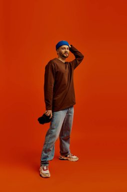 Şık bir genç adam, turuncu bir fona karşı şapkasıyla güvenle poz verir..