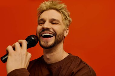 Neşeli genç adam bir mikrofon tutuyor, neşeyle şarkı söylerken gülümsüyor..