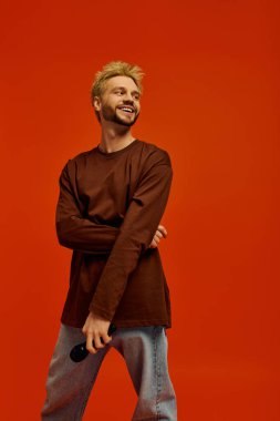 Karizmatik bir genç adam mikrofonla turuncu bir fona gülümsüyor..