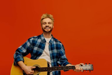 Neşeli genç bir adam gitarını çalar, mavi bir gömlek ve parlak bir gülümsemeyle..