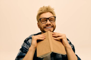 Gözlüklü neşeli genç bir adam neşeli bir şekilde kitabı kucaklıyor..