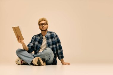 Yakışıklı genç bir adam yerde rahatça oturup, sakin bir mekanda kitap okuyor..