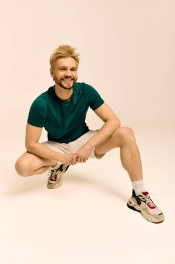 Yeşil gömlek ve şort giymiş yakışıklı genç adam, neşe içinde çömelmiş.