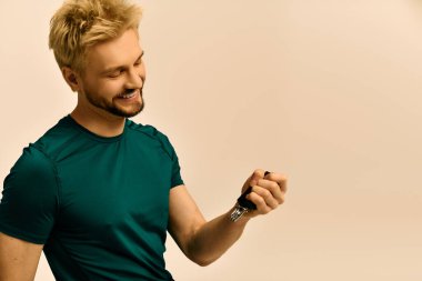 Sarı saçlı yakışıklı genç bir adam zarif saatine hayran, yumuşak ışıkta neşeyle gülümsüyor..